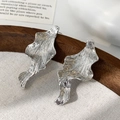 Détail de boucles d'oreilles vagues argentées irrégulières avec texture sur fond canevas - Argenté