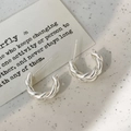 Dettaglio di orecchini a perno a forma di C intrecciati in argento su vassoio minimalista - Stile a Spirale Opaco / Argento