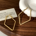 Detailed view of large golden rhombus earrings with a frosted finish on a wooden plate - Gold Small Square Earrings