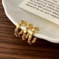 Macro detail of golden geometric cube beaded hoop earrings on a ceramic display - Gold