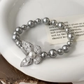 Gros plan d'un bracelet en perles élégant avec charm papillon brillant sur plateau céramique - Bracelet en Perles Papillon Gris (B-156)