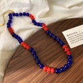 Dettaglio di collana con perline di vetro colorate e chiusura dorata su vassoio - Rosso/Blu Scuro