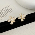 Dettaglio macro di orecchini a fiore dorati con zirconi pavé e perla bianca centrale - Borchie a fiori d'oro