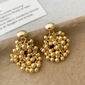 Detailed close-up of golden beaded tassel earrings on a textured paper background - Gold Tassel Stud Earrings