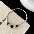 Gros plan d'un bracelet minimaliste en argent avec perles noires et barre ondulée - Style Perles Noires