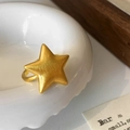 Primer plano de un anillo de estrella dorado con textura cepillada sobre un cuenco blanco - Dorado
