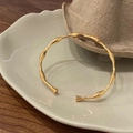 Gedetailleerde macro-opname van een gouden bamboe-armband op een decoratief keramisch dienblad - Bamboe Schakel Open Stijl / Goud