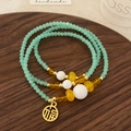 Detail eines grünen Kristall-Armbands mit goldenem Fu-Anhänger auf Holztablett - Grünes Kristall Mehrschicht-Armband