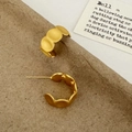Detalle de pendientes en forma de C de oro mate con textura ondulada sobre papel - Dorado Mate