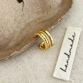 Detail einer goldfarbenen dreilagigen Ohrmanschette mit Perlenstruktur auf Papier - Gold