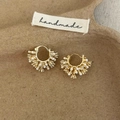 Close-up of golden hoop earrings featuring pearls and crystals on handmade paper tray - Gold