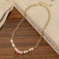 Détail d'un collier doré avec perles d'eau douce et pendentif cœur rouge sur bois - Cœur Rouge