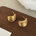 Nahaufnahme goldener strukturierter Ohrstecker mit Zirkonia auf einer Holzoberfläche - Gold