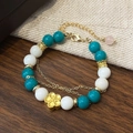 Dettaglio del bracciale di perle con pietre turchesi e pendente a fiore dorato su lino - Bracciale in pietra naturale verde