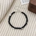 Detalle de pulsera de cuentas de ágata negra con dijes de mariposa plateados sobre tejido - Pulsera de Ágata Negra