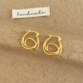 Detalle de pendientes de aro dorados multicapa sobre fondo de textura artesanal - Dorado