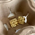 Makroaufnahme goldener quadratischer Ohrringe mit gewebter Textur auf mattem Metall - Gold
