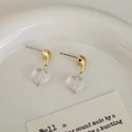 Détail de boucles d'oreilles cœur en verre transparent sur un plateau en céramique - Doré