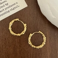 Close-up of golden irregular lava texture hoop earrings on a vintage wooden background - Gold