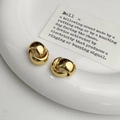 Detailed view of polished gold knot earrings displayed on a white ceramic plate - Gold