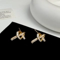 Close-up of golden knot earrings with pavé sparkling zircon stones on a black display - Gold Knot Stud Earrings