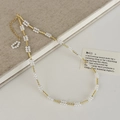 Dettaglio della collana con tubi dorati e perle su sfondo di libro in lino beige - Collana / Oro