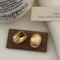 Dettaglio di orecchini ovali in oro opaco con texture spazzolata su base in legno - Oro Spazzolato (A-629)