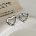 Dettaglio di eleganti orecchini a cuore cavo in argento su un vassoio di ceramica bianca - Argento
