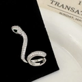 Macro detail of silver snake ear cuff with white cubic zirconia and green gemstone eyes - Silver