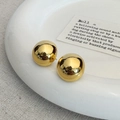 Detail van gouden bolvormige oorknopjes met spiegeleffect op wit keramisch bord - Goud