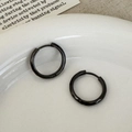 Detail van zwarte huggie hoop oorbellen gepresenteerd op een elegante esthetische achtergrond - Eenvoudige Ringstijl / Zwart