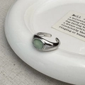 Dettaglio dell'anello d'argento con opale verde posto su un piatto di ceramica minimalista - Occhio di Gatto Verde Argentato (C-392银色)
