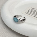 Dettaglio di un anello d'argento regolabile con opale azzurro su un vassoio di ceramica bianca - Occhio di Gatto Blu Argentato (C-392银色)