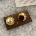 Pendientes vintage dorados con textura martillada sobre fondo de madera oscura - Dorado Mate