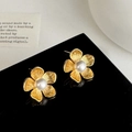 Dettaglio di orecchini a fiore dorati con perla centrale e texture metallica spazzolata - Oro