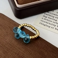 Detail of beaded gold ring with four faceted blue crystals on rustic wooden background - Gold Blue Glass Beads