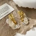Detailed macro of golden lava texture earrings with dangling white shell discs and luster - Gold