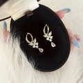 Detalle de pendientes de mariposa dorados con circonitas sobre un soporte de terciopelo - Dorado