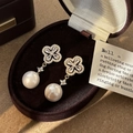 Detalle de pendientes de trébol con circonitas y perla en un joyero de terciopelo - Pendientes de Botón de Perla de Concha y Flor Dorada