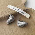 Macro di orecchini a spirale in argento appoggiati su un vassoio di carta artigianale - Argento