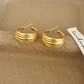 Dettaglio macro di orecchini a C dorati con nervature orizzontali e texture ricca - Oro