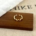 Macro shot of wavy gold ear cuff on dark wood with minimalist geometric texture - Gold