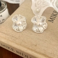 Detalle de pendientes de flor plateados con perla blanca sobre libro antiguo - Plateado