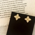 Macro shot of gold four-leaf clover stud earrings with white zircon pavé on a black display - Gold