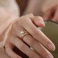 Anello incrociato dorato con perla e zirconi indossato da una modella in luce naturale - Anello a Croce con Perla di Conchiglia Dorata e Micro Intarsi