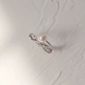 Dettaglio dell'anello con perla e fascia incrociata con zirconi su sfondo grigio elegante - Anello a Croce con Perla di Conchiglia Argentata e Micro Intarsi