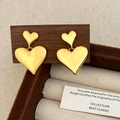 Detailed close-up of golden layered heart earrings on a dark wooden jewelry stand - Gold