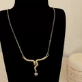 Dettaglio di una collana con ciondolo a serpente dorato e cristalli su supporto di velluto - Collana Piccola Serpente Oro (B-604)