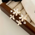 Detalle de pendientes florales de esmalte y circonitas sobre joyero de terciopelo beige - Flor Blanca