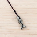 Dalmatian Jasper fish pendant with a woven cord necklace on a light wood background - Dalmatian Jasper